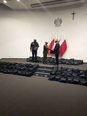 Mężczyzna podaje dłoń żołnierzowi na tle rozłożonych na podłodze paczek