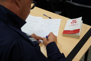 policjanci rozwiązują pisemnie kazus siedząc na krzesłach przy ławkach