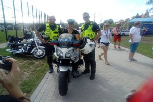 Jedna z uczestniczek festynu na policyjnym motocyklu w asyście policjantów