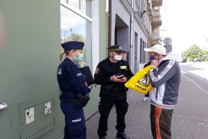 Osoba otrzymuje maseczkę ochroną od policjanta i strażnika miejskiego