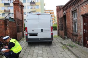 Policjant prowadzi oględziny roweru i samochodu na miejscu wypadku.