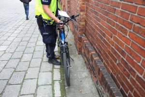 Policjant prowadzi oględziny roweru i samochodu na miejscu wypadku.