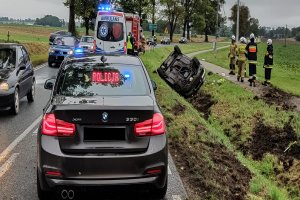 Nieznakowany radiowóz BMW, za ni Straż Pożarna, a po prawej stronie w rowie leżący na dachu volkswagen Passat.