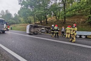 Strażacy stoją obok leżącego na boku mercedesa