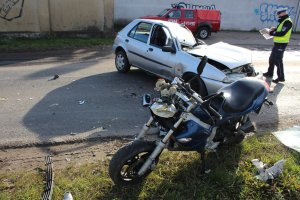 Policjant sporządzający dokumentację stojąc obok forda i rozbitego motoroweru.