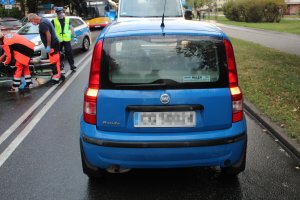 Tył niebieskiego samochodu stojącego na jezdni. Po lewej stronie pojazdu pracownicy pogotowia i policji