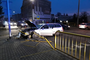 Rozbity samochód Volkswagen na barierkach przy chodniku.