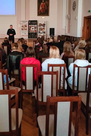 na auli liceum ogólnokształcącego stoi policjant zwrócony przodem do uczniów, którzy siedzą na krzesłach