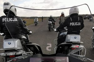 na zdjęciu widać dwóch policjantów siedzących na motocyklach, na głowach mają założone kaski, policjanci odwróceni są tyłem. W tle widać policjantów jadących na motocyklach