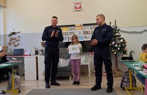 policjanci przy dziecku prezentującym swoją pracę