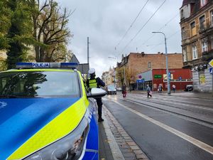 policjant stoi przy radiowozie i  nadzoruje ruch drogowy