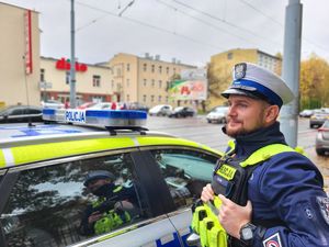 policjant stoi przy radiowozie i  nadzoruje ruch drogowy