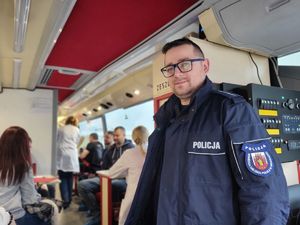 Policjant w okularach granatowej kurtce uśmiech się do aparatu.