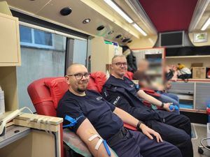 Dwóch policjantów siedzi na czerwonych fotelach podczas pobierania krwi.