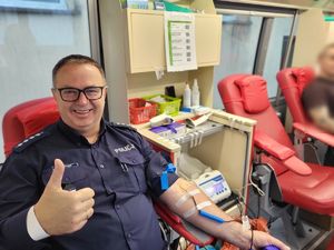 Uśmiechnięty policjant oddaje krew i pokazuje kciuk w górę.