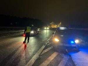 Radiowóz z włączonymi sygnalizatorami nadającymi barwę niebeską. Policjant na drodze z latarką do zatrzymywania pojazdów koloru czerwonego.