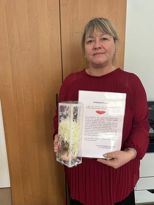 Podziękowanie: Portret kobiety w bordowej bluzce, która trzyma w rękach biały arkusz z napisem "PODZIĘKOWANIE" oraz ozdobne pudełko z upominkiem.