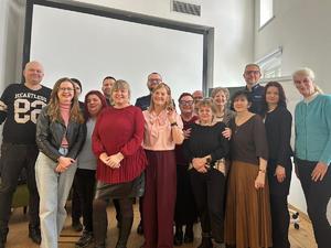 Zdjęcie grupowe: Wszyscy uczestnicy spotkania – funkcjonariusze policji oraz osoby cywilne – stoją razem do wspólnego, pamiątkowego zdjęcia na tle białego ekranu.