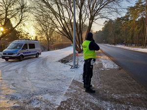 policjant w trakcie pomiaru prędkości stoi przy krawędzi jezdni